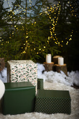 Christmas gift boxes on a white fluffy sofa under green fir trees in which Christmas lights are installed, which create a bokeh effect.