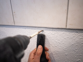 Drilling a hole into a wall in an apartment. Close up of the drill bit rotating. Holding a vacuum...