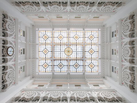 Directly from below view of large skylight with stained glass decor on white library with carvings