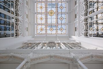 Directly from below view of large skylight with stained glass decor on white library with carvings