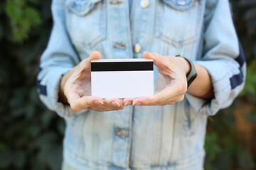 Woman in jeans jacket holding credit card against green plants wall background