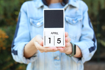 Woman in denim jacket holds white block wooden calendar with date April 15 outdoors