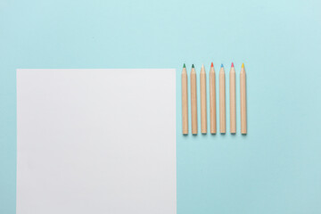 Wooden colored pencils and paper sheet on blue background. Creativity, art