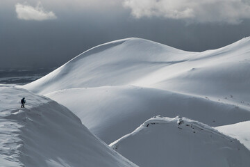High angle from above view of silhouette unrecognizable hiker walking on beautiful snow covered mountain range against cloudy sky during winter vacation at Japan