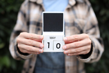 Woman holds calendar with the date May 10 outdoors.