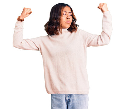 Young beautiful mixed race woman wearing winter turtleneck sweater showing arms muscles smiling proud. fitness concept.