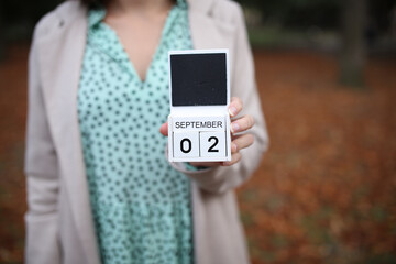 Woman holds calendar with the date september 2 outdoors.