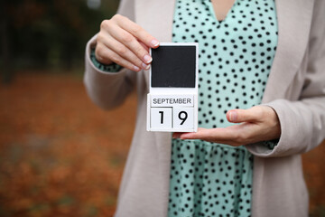 Woman holds calendar with the date september 19 outdoors.