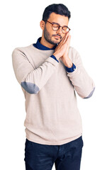 Young handsome hispanic man wearing elegant clothes and glasses sleeping tired dreaming and posing with hands together while smiling with closed eyes.