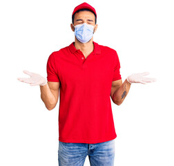 Young handsome hispanic man wearing delivery uniform and medical mask celebrating mad and crazy for...