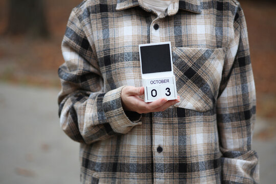 Woman in warm shirt holds calendar with date October 03 outdoors in autumn park