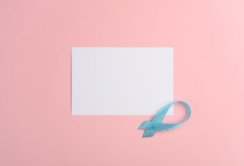 White blank sheet of paper and blue awareness ribbon on pink background