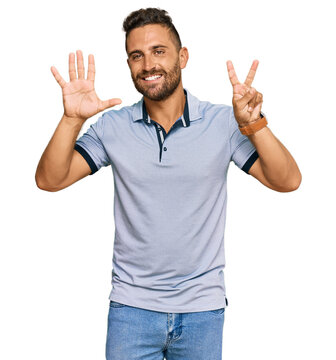 Handsome man with beard wearing casual clothes showing and pointing up with fingers number seven while smiling confident and happy.