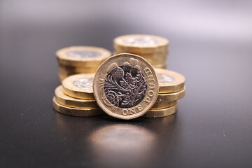 New one pound coins on a dark background.  Piles of coins and one standing in front.  British coin....