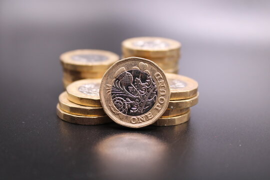 New one pound coins on a dark background.  Piles of coins and one standing in front.  British coin.  British pound. Dark background.  Black background