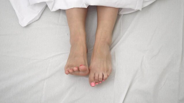 woman pulling blanket stretching legs in bed joyfully moving fingers in the morning