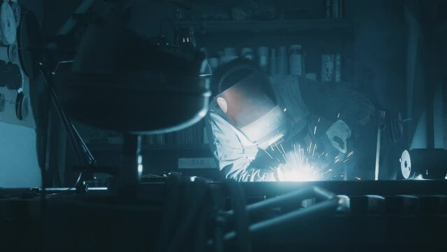 A man works with a welding machine at a factory. A welder welds metal in a workshop. Sparks fly from hot metal. The man worked hard on the steel. Close-up slow motion in the garage. 4K video