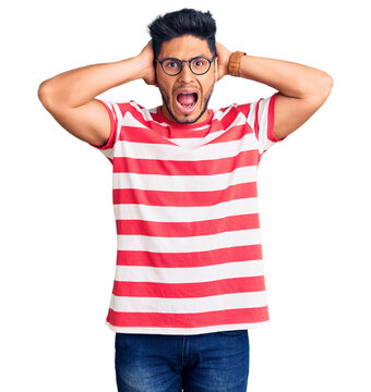 Handsome latin american young man wearing casual clothes and glasses crazy and scared with hands on head, afraid and surprised of shock with open mouth