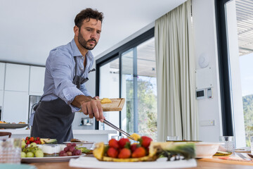 From below of bearded Male chef in apron putting pineapple slices on plate placed on table in modern dining room