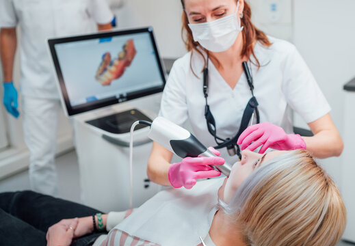 Dentist female doctor in uniform using intraoral 3D dental scanner Machine for clear aligners production. Dental clinic patient visit modern medical ward. Health teeth care, medicare industry concept.