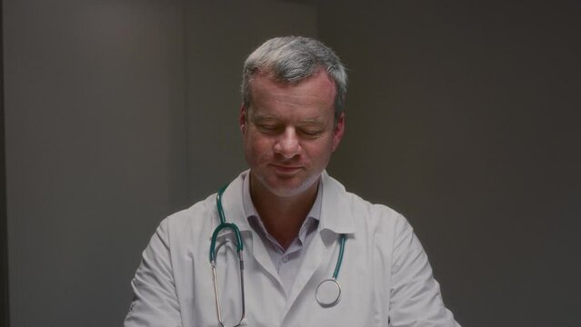 Medic with grey hair involved in discussion with client opening up about health related concerns. Doctor showing agreement by nodding head during conversation in clinic slow motion