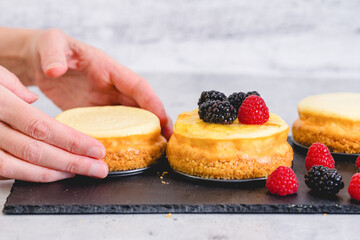 Mini cheesecakes close-up on the kitchen table, woman hands. Decorating cheesecakes with fresh berries