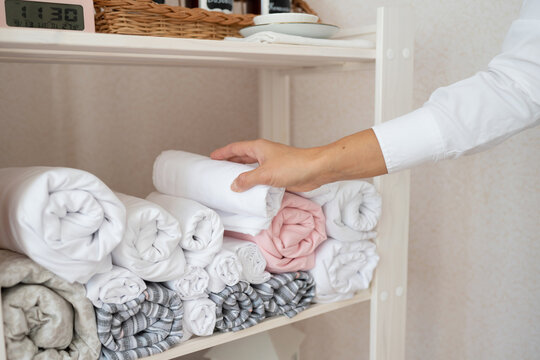 Crop hands of anonymous female massage therapist arranging clean rolled up white towels on shelf while working in luxurious spa salon