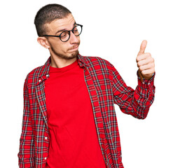 Hispanic young man wearing casual clothes looking proud, smiling doing thumbs up gesture to the side