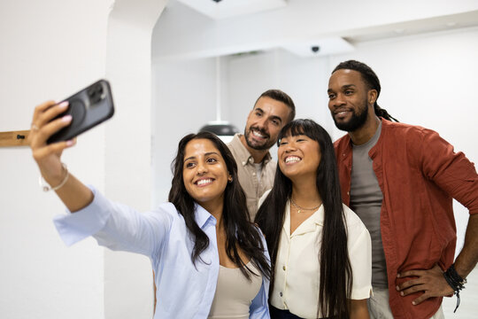 Cheerful colleagues taking selfie through phone in office