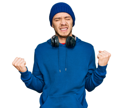 Hispanic young man wearing sweatshirt and wool hat very happy and excited doing winner gesture with arms raised, smiling and screaming for success. celebration concept.