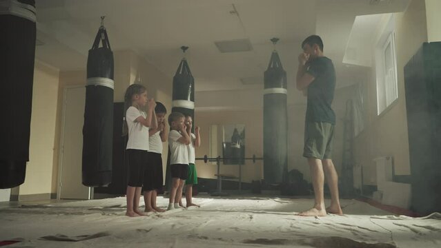 Children do blocks with trainer in martial arts school. Little boxing students learn self-defence under instructor control in gym slow motion