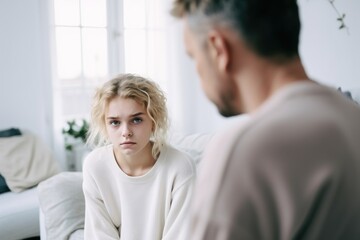 Оffended teenager daughter and middle aged father argument, сlose up upset man in front and girl behind sit at sofa after quarrel at home, family conflict concept, problems of adolescence