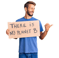 Handsome blond man with beard holding there is no planet b banner pointing thumb up to the side smiling happy with open mouth