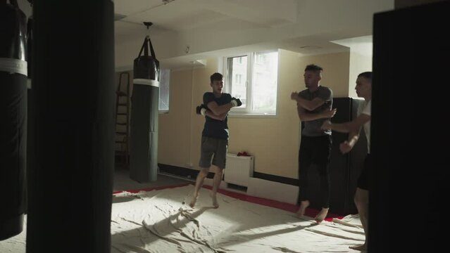 Athletes run sidestepping and warming up arms in fighting gym. Fighters do active workout in mixed martial arts club slow motion. Body development