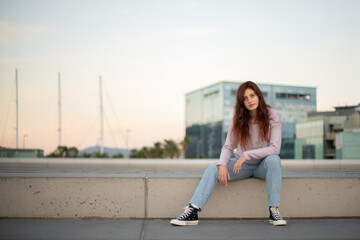 Young woman in casual clothes posing in front of an urban setting at sunrise.