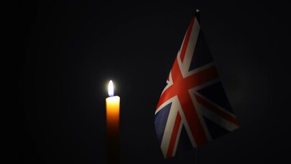 The national flag of Great Britain and a burning wax candle on a dark background. Free space for text. - Powered by Adobe