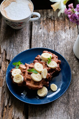 chocolate Belgian waffles with banana. wooden background, blue plate.