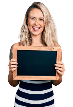 Young blonde woman holding blackboard sticking tongue out happy with funny expression.