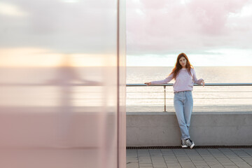 Obraz premium Young woman posing in front of the sea reflected on a pink wall. Dramatic sky.