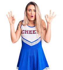 Young beautiful blonde woman wearing cheerleader uniform looking surprised and shocked doing ok...