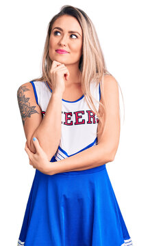 Young beautiful blonde woman wearing cheerleader uniform with hand on chin thinking about question, pensive expression. smiling and thoughtful face. doubt concept.