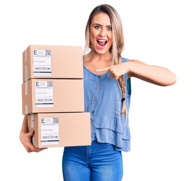 Young beautiful blonde woman holding delivery boxes smiling happy pointing with hand and finger