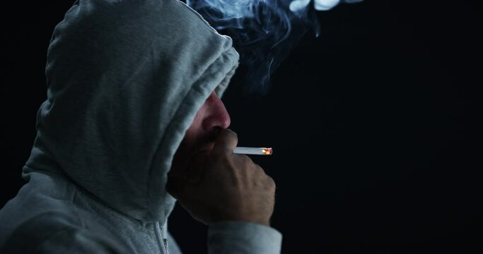 Man, smoke and cigarette with hood in dark, danger and risks of tobacco, nicotine and drugs in mockup. Male person, hiding and relief in bad habits, stress and addiction by black background in studio