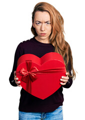Young caucasian woman holding valentine gift skeptic and nervous, frowning upset because of problem. negative person.