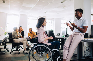 Businesswoman with disability listening to multiracial colleague at office. - obrazy, fototapety, plakaty