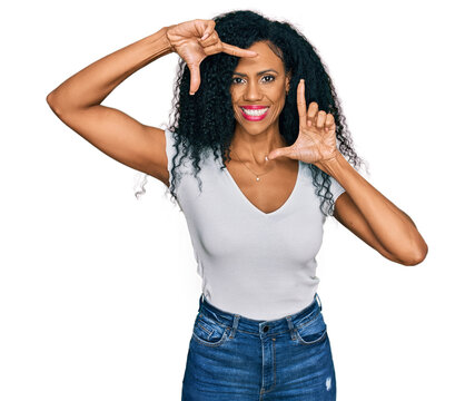 Middle age african american woman wearing casual white t shirt smiling making frame with hands and fingers with happy face. creativity and photography concept.