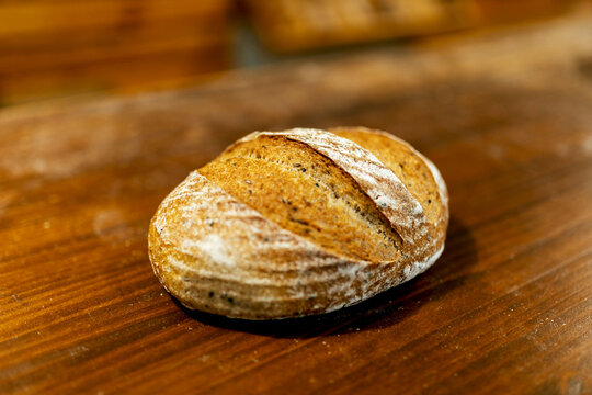 Closeup of freshly baked tasty loaf of bread with crispy crust placed on wooden table in kitchen at bakehouse - Powered by Adobe