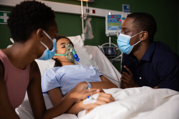 African parents wearing masks sitting in ward near their daughter in bad condition wearing oxygen mask.