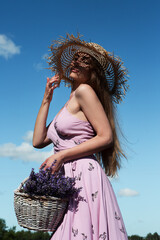Young sexy beautiful woman in a straw hat with a basket enjoys the scents of flowers in a lavender...