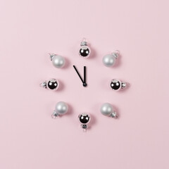 Clock hands with decorative baubles on pink background. Minimal New Year or Christmas concept.